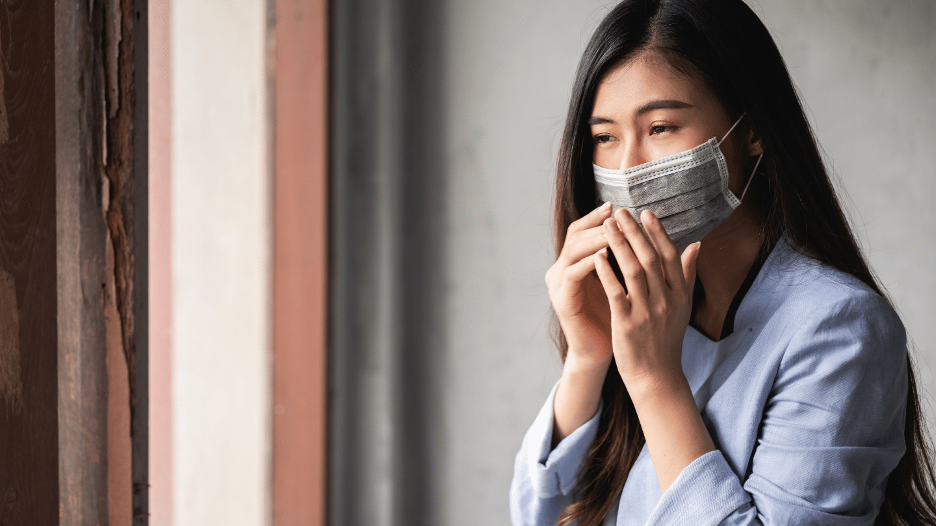 Woman with a face mask experiencing both COVID-19 and flu symptoms