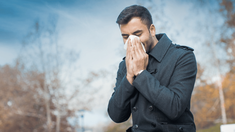 Man outdoors blowing his nose, dealing with a runny nose during cold weather